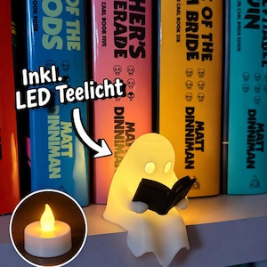 May include: A small, off-white, ghost-shaped figurine reading a black book, illuminated from within. A white arrow points to the text Inkl. LED Teelicht, with a circular inset showing a glowing, battery-operated LED tea light candle.