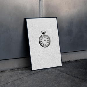 Puede incluir: Impresión en blanco y negro enmarcada de un reloj de bolsillo. La esfera del reloj presenta números romanos y delicadas manecillas. La impresión está apoyada contra una pared texturizada, creando una estética vintage.