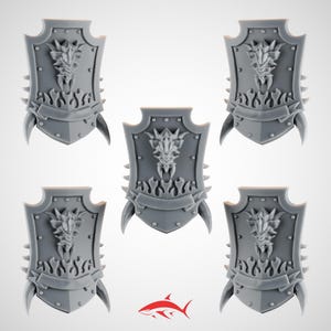 May include: Five gray miniature shields with a dragon head design. Each shield has a banner, spikes, and a pair of horns. The shields are likely for tabletop gaming or miniature wargaming.