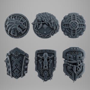 Peut inclure: Ensemble de six mini-boucliers gris avec des motifs complexes. Les boucliers présentent divers motifs, dont une tête de loup, de la fourrure et des motifs géométriques. Ces boucliers décoratifs sont probablement destinés aux jeux de société ou à l'exposition.