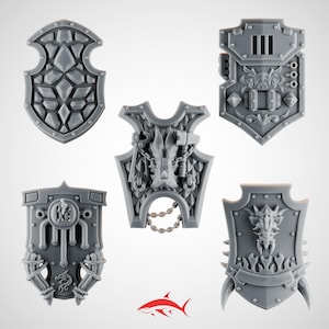 May include: Five gray plastic shields with intricate designs. The shields feature various shapes and details, including geometric patterns, dragon heads, and mechanical elements. The shields are likely for miniature figures or tabletop games.