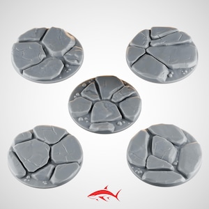 Op de afbeelding: Vijf grijze, cirkelvormige bases met een gebarsten steenstructuur. Elke basis is samengesteld uit verschillende onregelmatige steenvormen, met kleine kiezeldetails langs de randen. De bases zijn ontworpen voor miniatuurfiguren.