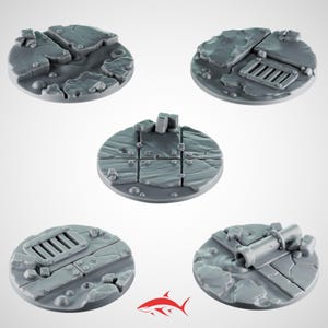 May include: Five gray, circular miniature bases with textured, cracked, and broken stone designs. One base features a metal grate, another a pipe, and others have various rock formations. The bases are designed for miniature figures.