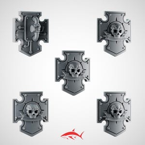 Könnte beinhalten: Fünf graue Kunststoffschild-Miniaturen. Vier Schilde zeigen einen Totenkopf mit Lorbeerkranz und Banner. Ein Schild hat ein mechanisches Design. Die Schilde haben eine Kreuzform mit spitzem Boden.