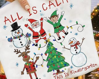 Könnte beinhalten: Weißer Kissenbezug mit Weihnachtsmotiv und dem roten Text "ALL IS CALM" und "Just Kidding, This Is Kindergarten". Das Design zeigt Cartoon-Illustrationen eines Schneemanns, Weihnachtsmanns, Elfen, Rentiers, Weihnachtsbaums und eines zweiten Schneemanns.