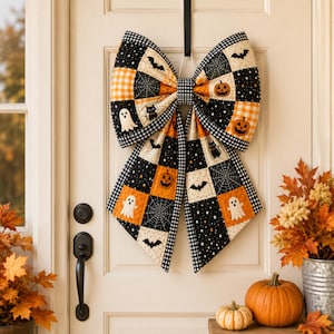May include: A large decorative bow made of quilted fabric featuring a patchwork pattern of black, orange, and white squares. The design includes motifs of ghosts, pumpkins, black cats, bats, and spiderwebs, finished with a black and white gingham trim.