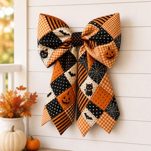May include: A large decorative bow made of quilted fabric featuring a patchwork pattern of orange and black squares. The design includes motifs of jack-o'-lanterns, black cats, bats, spiderwebs, polka dots, and gingham checks in a seasonal theme.