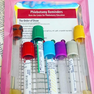 May include: A selection of blood collection tubes with various coloured stoppers, such as red, green, blue, and purple, within a pink plastic sleeve. The tubes are labelled with text and measurements, for phlebotomy.