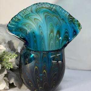 Può includere: Un vaso decorativo in vetro con bordo a balze. Il vaso presenta una miscela di colori blu, verde acqua e giallo in un motivo a vortice. Il vaso ha una base rotonda e una parte superiore svasata, creando un design unico e artistico.