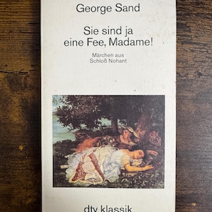 May include: A vintage paperback book titled "Sie sind ja eine Fee, Madame!" by George Sand. The cover features an illustration of a woman in a white dress lying down, with two other figures in the background. The book is from the "dtv klassik" series.