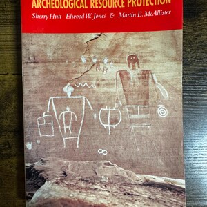 May include: A book titled "ARCHEOLOGICAL RESOURCE PROTECTION" with a red banner and a tan cover. The cover features ancient rock art drawings of human figures and symbols. Authors' names are listed below the title.