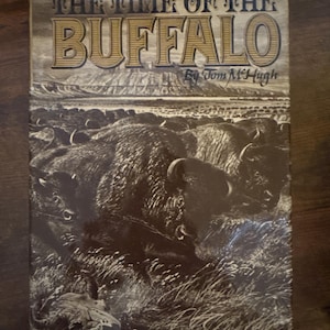 May include: A vintage book titled "The Time of the Buffalo" by Tom McHugh. The cover shows a sepia-toned illustration of a herd of buffalo in a grassy field with a mountain range. The title is in large, ornate lettering.