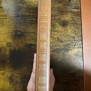 Puede incluir: Un libro antiguo de tapa dura titulado "The Hidden Years" de John Oxenham, parte de la serie Family Classics. El libro tiene una cubierta marrón con letras doradas y elementos decorativos. El lomo es visible, mostrando el título y el autor.