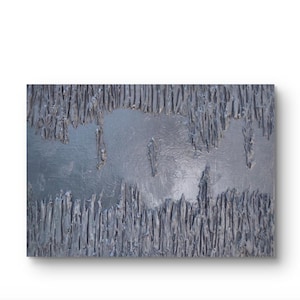 May include: Abstract textured artwork in shades of gray and silver. The piece features a rough, layered surface with vertical and horizontal elements, creating a dynamic visual effect. The artwork is mounted on a white background.