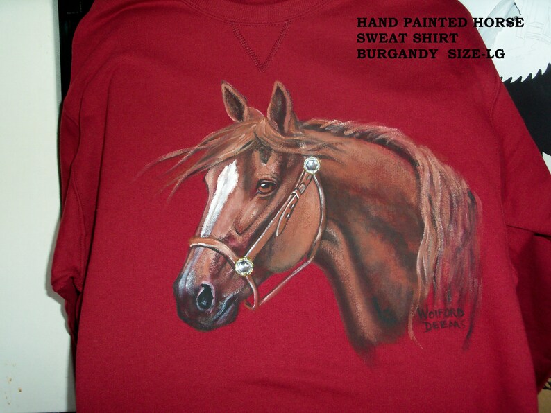 May include: Burgundy sweatshirt with a hand-painted image of a brown horse's head. The horse is wearing a brown leather bridle with silver accents. The text "HAND PAINTED HORSE SWEAT SHIRT BURGANDY SIZE-LG" is printed on the top of the sweatshirt.