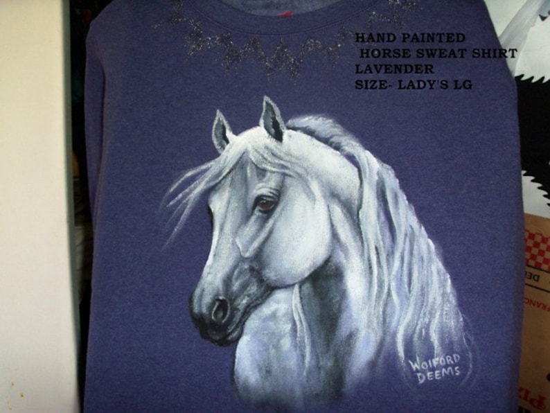 May include: Hand-painted lavender sweatshirt with a white horse design. The shirt says "HAND PAINTED HORSE SWEAT SHIRT LAVENDER SIZE-LADY'S LG" and is signed "WOIFORD DEEMS".