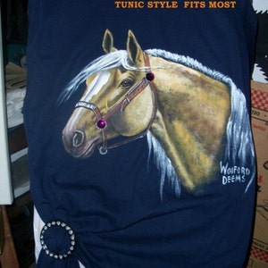 May include: A navy blue t-shirt with a hand-painted image of a horse's head. The horse is light brown with a white mane and a pink bridle. The shirt has a tunic style and says "HAND-PAINTED HORSE T-SHIRT SIZE LG TUNIC STYLE FITS MOST" and "WOIFORD DEEMS" in white text.