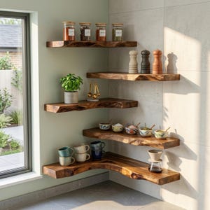 Op de afbeelding: Vijf trapsgewijze hoekplanken van natuurlijk hout met boomstamranden. De planken bevatten glazen kruidenpotjes, drie houten zout- en pepermolens, een groene plant in pot, een gouden maatlepelset, kleine schaaltjes met patronen, keramische mokken en een glazen filter.