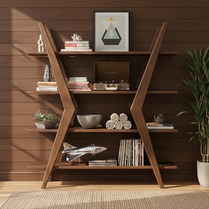 Op de afbeelding: Een houten boekenplank met een hoekig ontwerp, gevuld met boeken, decoratieve items en een platenspeler. De planken tonen een verscheidenheid aan objecten, waaronder een modelvliegtuig, een terrarium en opgerolde handdoeken. De achtergrond is een houten muur.