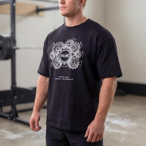 May include: Black short-sleeved t-shirt featuring a white graphic of interlocking gears and the word "VOLUME". The text "STRYDE // 007 CONTROL THE VARIABLES" is printed below the graphic. The shirt is made of a soft material.