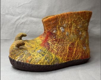May include: A handmade felt slipper in shades of yellow, orange, and red, with a dark brown sole. The slipper has a unique, curled toe design. The texture of the felt is visible, showcasing the craftsmanship of the item.