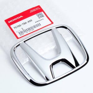 May include: A chrome Honda emblem with a shiny, reflective surface. The emblem is in the shape of the Honda logo and is accompanied by a red and white label with the text "HONDA" and part information.