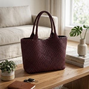 May include: A deep burgundy tote bag featuring a woven texture throughout the exterior. The bag has two matching woven handles attached to the top, a rectangular base, and an open main compartment. The design is consistent in color and pattern.