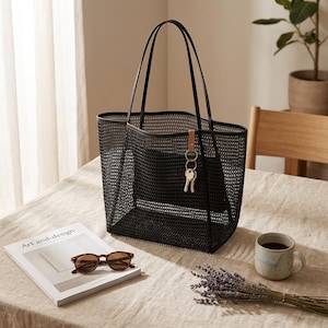 May include: A black mesh tote bag with two thin shoulder straps and a rectangular base. A small tan leather tab is attached to the top rim, holding a silver metal keyring with two keys. The bag features a consistent grid-like pattern throughout.