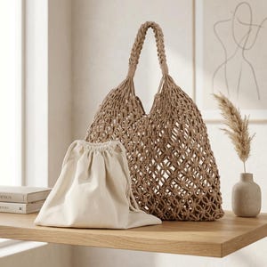 Könnte beinhalten: Eine beige Makramee-Tragetasche mit geflochtenem Griff und offenem Knotenmuster, begleitet von einem separaten, cremefarbenen Beutel mit Kordelzug. Die Tasche hat eine strukturierte, dreieckige Form und besteht aus dicker, strukturierter Kordel.