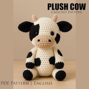 Puede incluir: Una vaca de peluche tejida a ganchillo con manchas negras y blancas, orejas negras y pequeños cuernos. La vaca tiene un hocico beige y está sentada. El texto "PLUSH COW CROCHET PATTERN" está en la parte superior y "PDF PATTERN | ENGLISH" en la inferior.