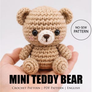 May include: A crocheted mini teddy bear in tan yarn with black safety eyes and a white muzzle. The bear has small, rounded ears and is sitting with its arms and legs outstretched. The text "MINI TEDDY BEAR" is displayed below the bear.