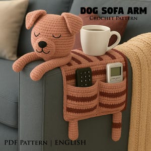 Puede incluir: Reposabrazos de sofá de perro tejido a ganchillo con dos bolsillos, que contiene un mando a distancia y un temporizador digital. La cabeza del perro está al final del reposabrazos. El texto "DOG SOFA ARM CROCHET PATTERN" está en la parte superior.