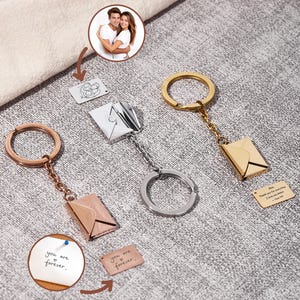 May include: Keychains with envelope pendants in rose gold, silver, and gold. Each keychain has a ring and chain. One keychain has the text "you are forever" on a small card. Another has the text "Thank you for everything I love you more..." on a small card.