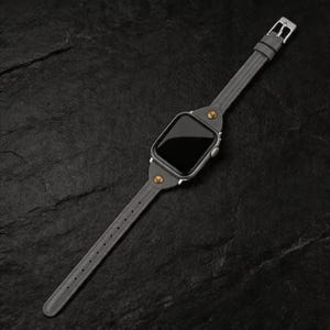 May include: A gray leather watch band with a silver buckle and a silver watch face. The band is secured with brass-colored rivets. The watch face is black.