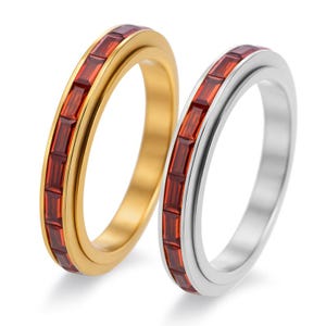 Könnte beinhalten: Zwei Ringe, einer goldfarben und einer silberfarben, werden gezeigt. Beide Ringe haben ein Band aus rechteckigen, tiefroten Edelsteinen. Der goldfarbene Ring hat eine polierte Oberfläche, während der silberfarbene Ring eine helle, reflektierende Oberfläche hat.