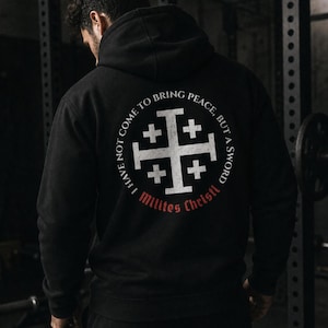 May include: A black hooded sweatshirt featuring a white graphic on the back. The design includes a Jerusalem cross surrounded by the text I HAVE NOT COME TO BRING PEACE, BUT A SWORD and the red text Milites Christi printed below the circle.