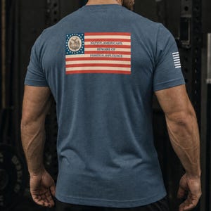 May include: A heathered blue short-sleeve t-shirt featuring a graphic on the back of a modified American flag with red and white stripes and a blue canton containing stars and a seal. The text reads NATIVE AMERICANS BEWARE OF FOREIGN INFLUENCE.