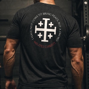 May include: A charcoal grey short-sleeve t-shirt featuring a white Jerusalem cross graphic on the back. The text "I HAVE NOT COME TO BRING PEACE, BUT A SWORD" circles the cross, with the red text "MILITES CHRISTI" printed underneath the design.
