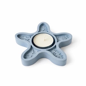 May include: A light blue, star-shaped candle holder with a white candle in the center. The holder has decorative cut-out patterns. The candle holder is made of a solid material.
