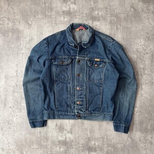 May include: A medium-wash blue denim jacket featuring a classic fold-over collar, a full-length button-front closure with metallic buttons, two chest pockets with buttoned flaps, and two lower vertical welt pockets with long-sleeve cuffs.
