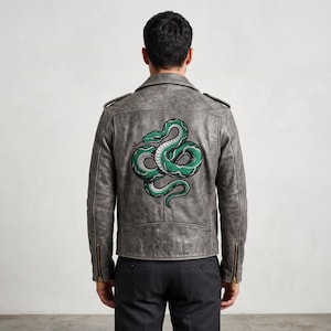 May include: A grey leather motorcycle jacket featuring a large, coiled green and white snake embroidery on the back. The jacket includes shoulder epaulets, long sleeves with gold-toned metal zips at the cuffs, and a structured back panel design.