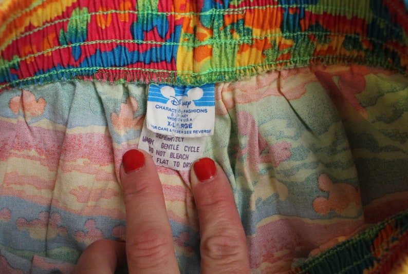 May include: A white tag with blue text attached to a colorful fabric. The tag reads "Character Fashions Disney Made in U.S.A. X-Large For care & other see reverse" and "Defenitiely Wash Gentle Cycle Do Not Bleach Flat to Dry".