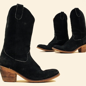 May include: A pair of black suede cowboy boots with a wooden heel. The boots have a pointed toe and a classic cowboy boot design.
