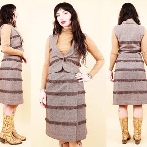 Op de afbeelding: Een vintage bruin tweed rokpak met bijpassend vest. De rok en het vest zijn versierd met horizontale franjes. De outfit wordt gecombineerd met een beige coltrui en laarzen met patroon, wat een retro esthetiek creëert.