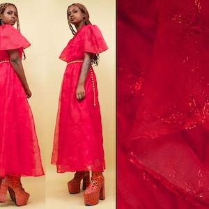 May include: A red, sheer maxi dress with a ruffled neckline and short sleeves. The dress has a gold belt and the model is wearing platform shoes.