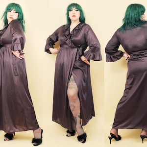 May include: A long, dark brown satin robe with a ruffled collar and long sleeves. The robe is tied at the waist with a sash and has a slit up the front. The model is wearing the robe with a pair of black heels.