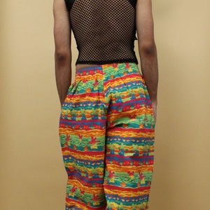 May include: A person wearing black mesh sleeveless top with a black collar and colorful patterned pants. The pants have a horizontal stripe pattern with red, orange, yellow, green, and blue colors.
