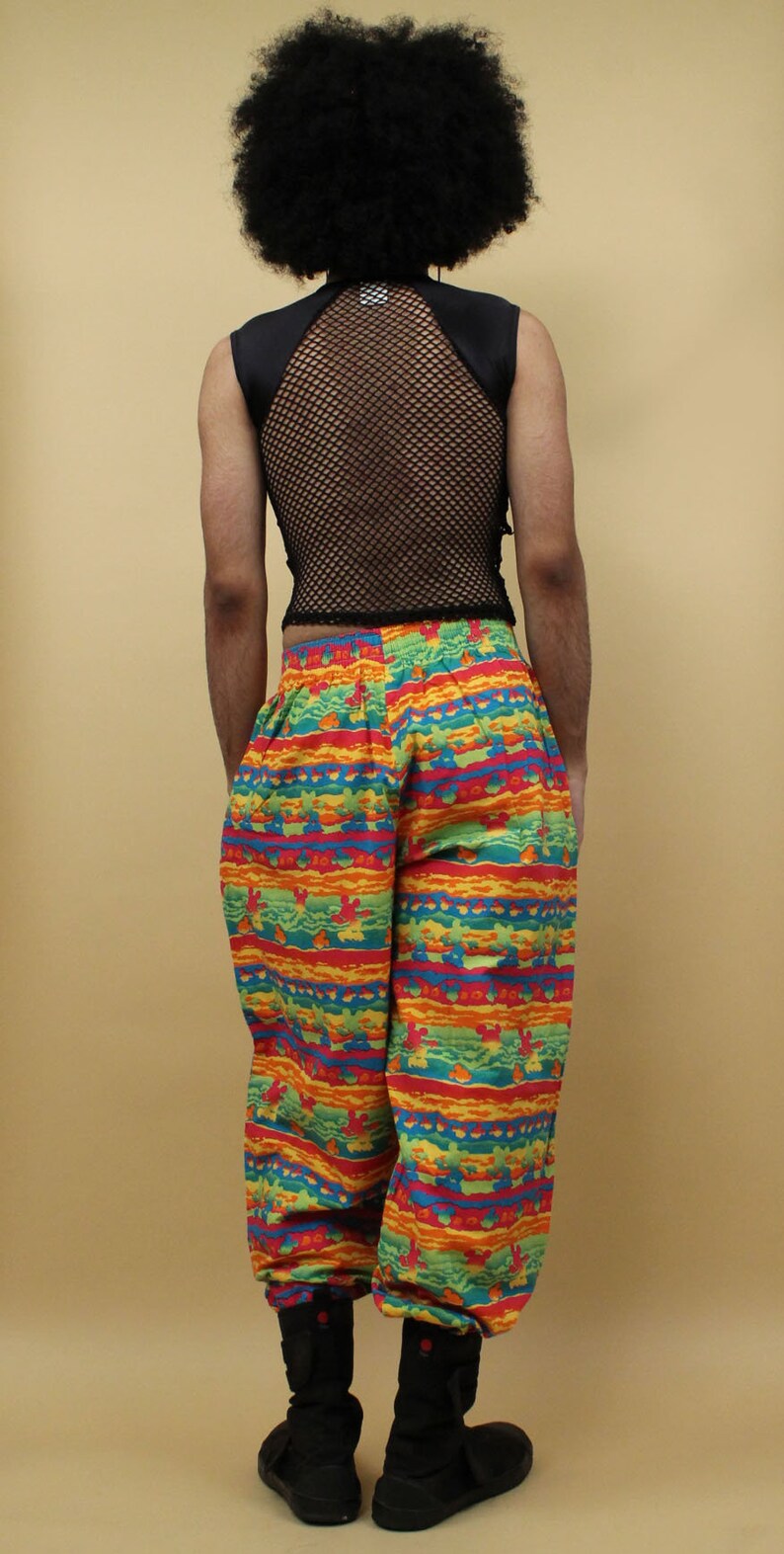 May include: A person wearing black mesh sleeveless top with a black collar and colorful patterned pants. The pants have a horizontal stripe pattern with red, orange, yellow, green, and blue colors.