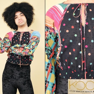 May include: A black and white polka dot blouse with a colorful patchwork design on the sleeves. The blouse has a tie at the neck and a ruffled hem. The brand name "KOOS VAN DEN AKKER, NEW YORK" is printed on the bottom of the image.