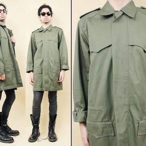 Può includere: Una lunga giacca in stile militare di colore verde oliva con chiusura a bottoni, due grandi tasche a lembo e un colletto. La giacca ha una vestibilità rilassata ed è realizzata in un tessuto di cotone resistente.